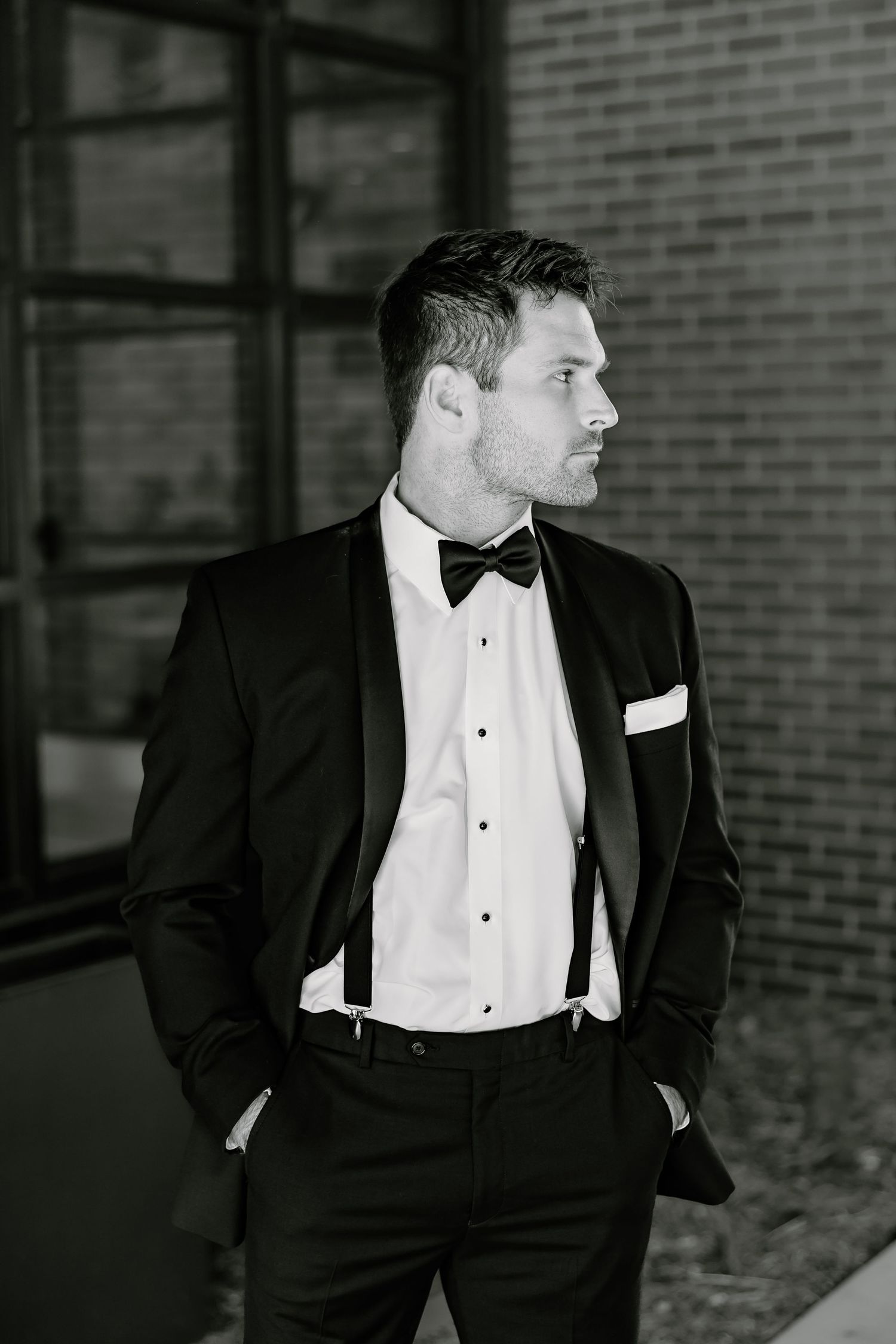 A black and white portrait of a groom in formal attire against an architectural backdrop.
