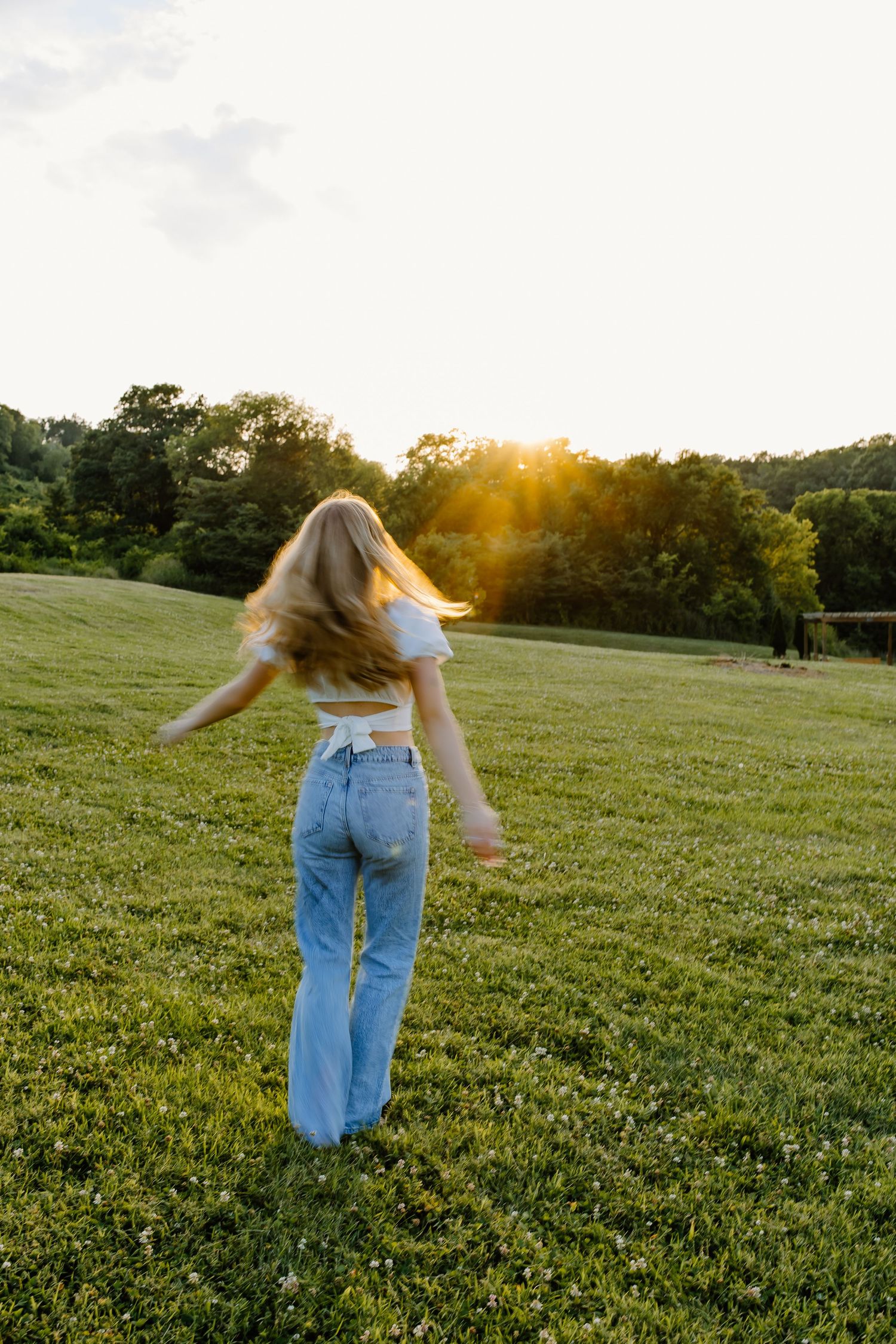 Person in jeans dancing freely in a sunlit meadow at golden hour.