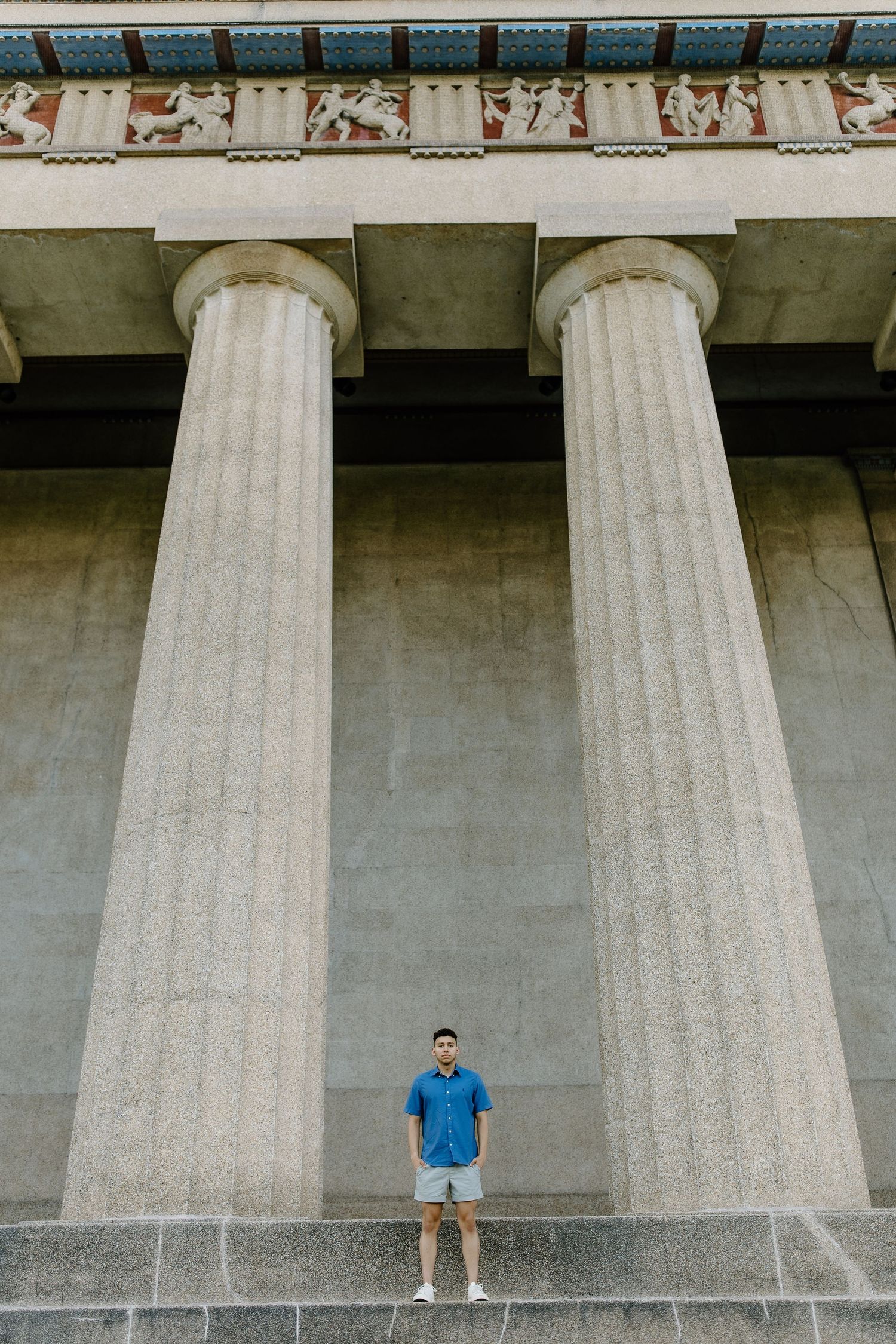 Person standing between massive classical columns wearing blue casual attire.