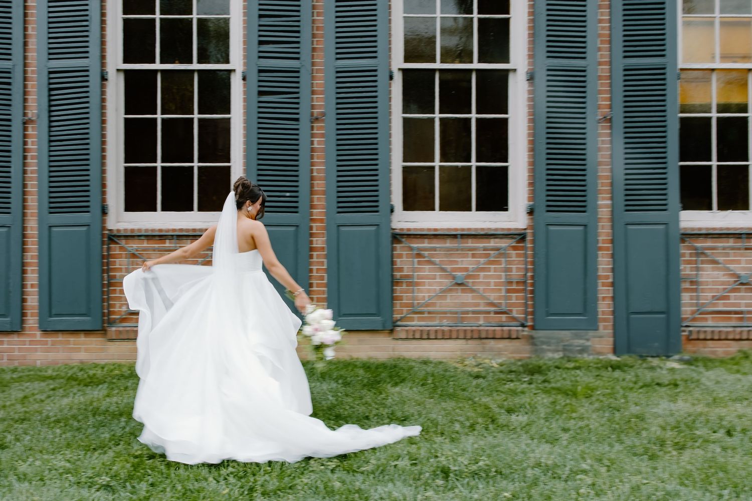 Bride in flowing white dress twirling against historic building with blue shutters.