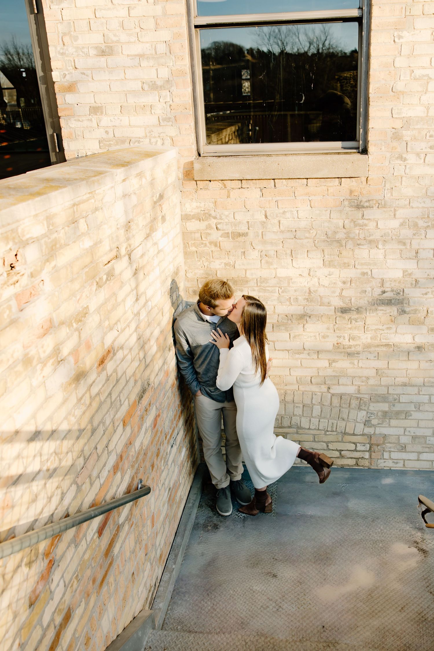 A couple sharing an intimate moment against a light brick wall in an urban setting.