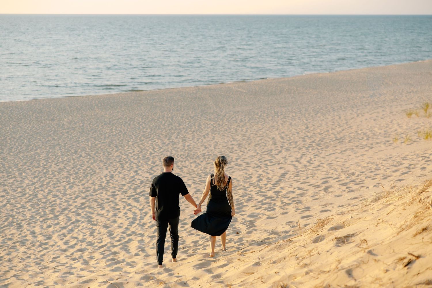 Couple walking hand in hand on a pristine sandy beach at sunset.