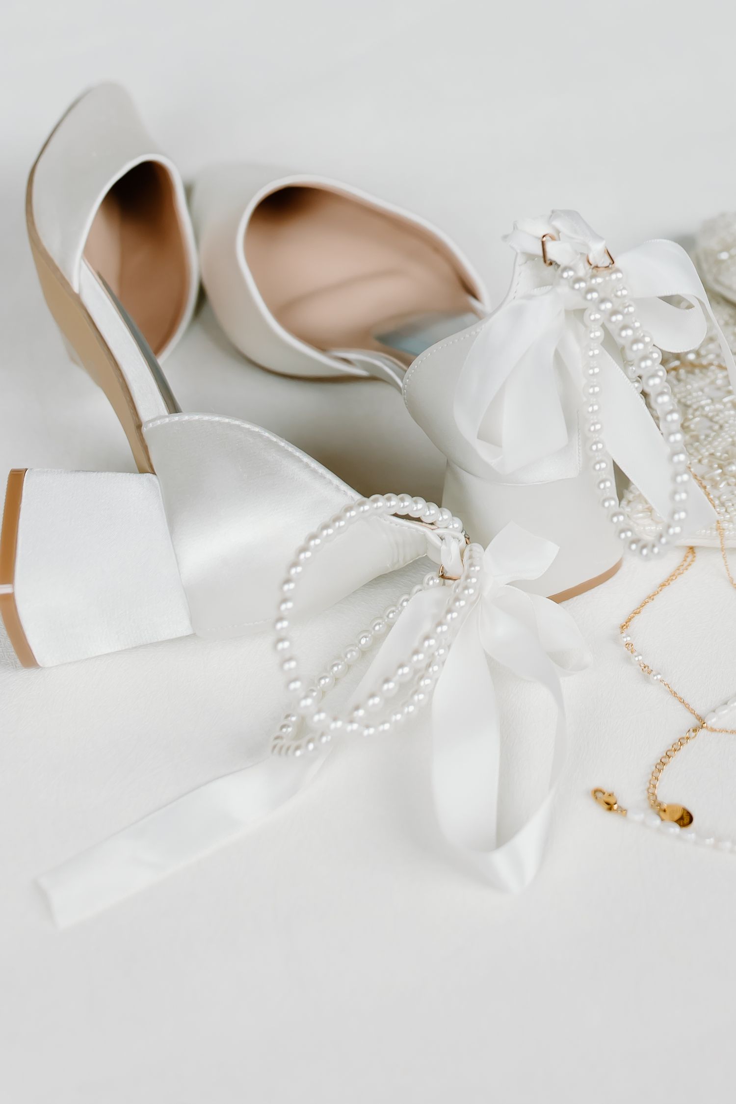 Elegant white bridal shoes with pearl accessories arranged on light background.