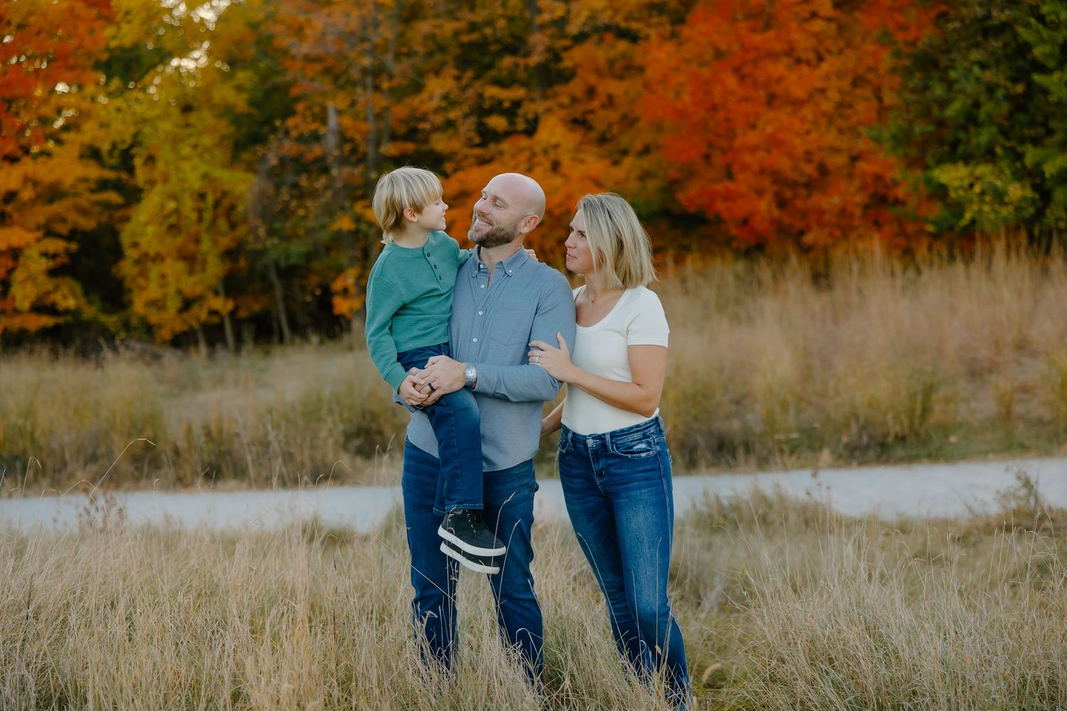 Family members share a candid moment in a field surrounded by fall colors.