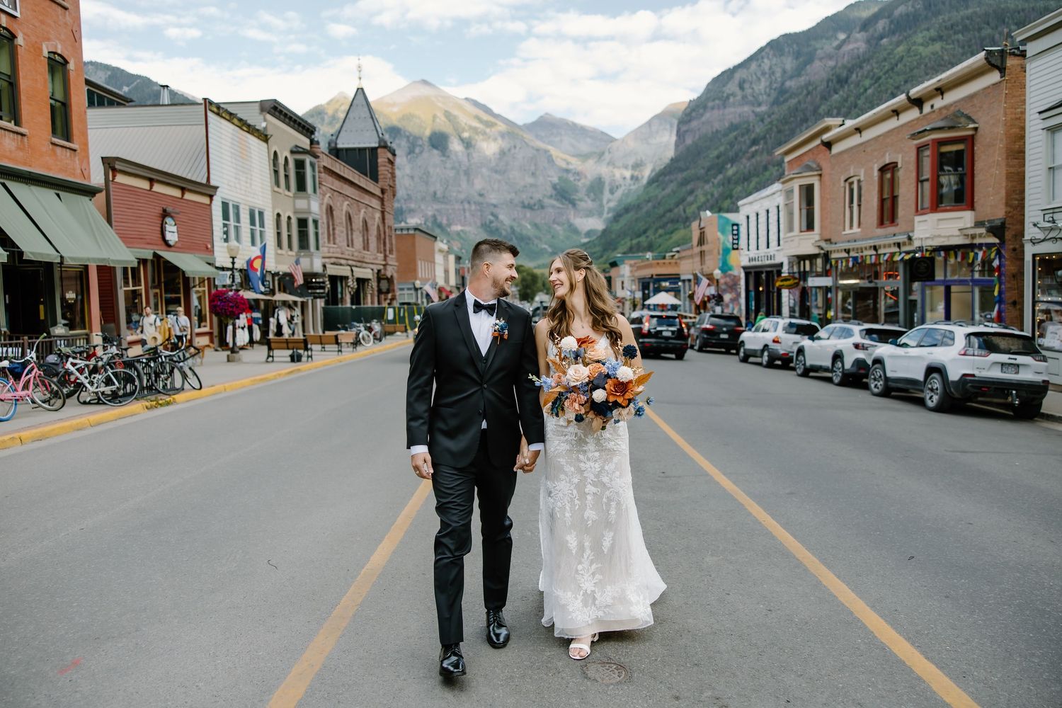 A wedding couple walks down the center of a picturesque mountain town street.
