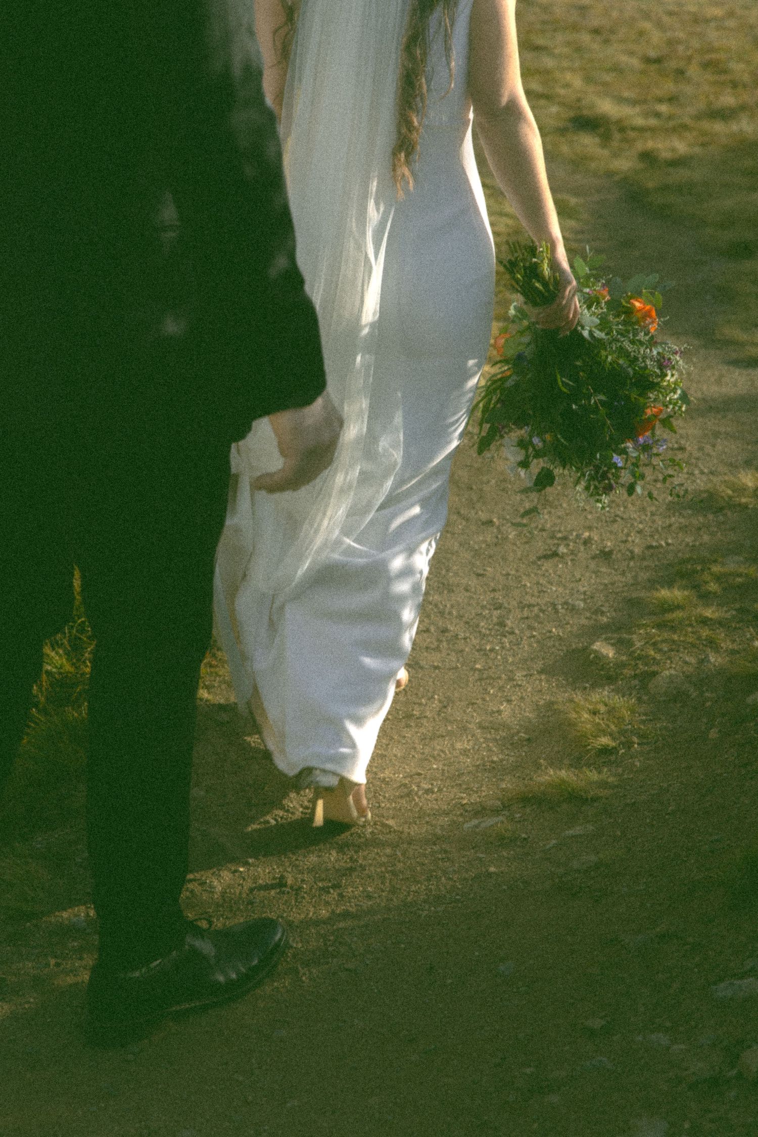 A couple's feet walking along a dirt path with sunlit foliage in the background.