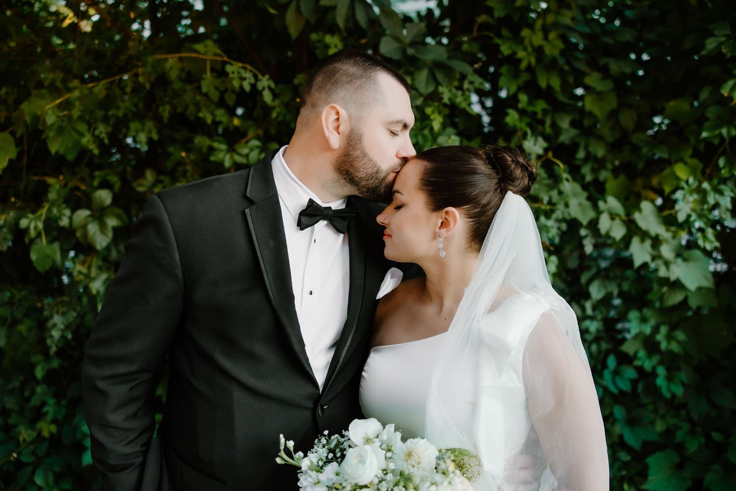 Intimate wedding portrait in front of lush green garden wall.