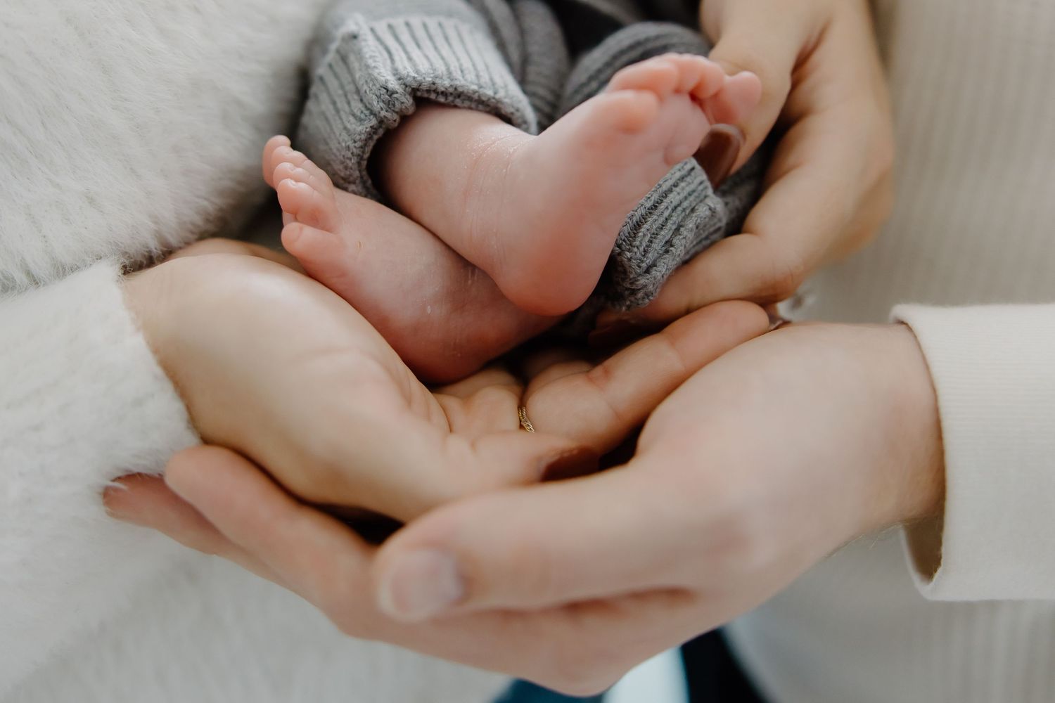 Gentle close-up of hands cradling a baby in soft natural lighting.
