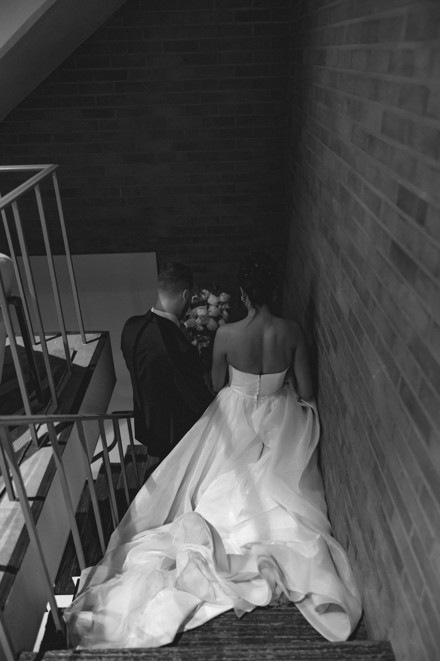 White wedding dress train flowing down dark wooden stairs in dramatic lighting.