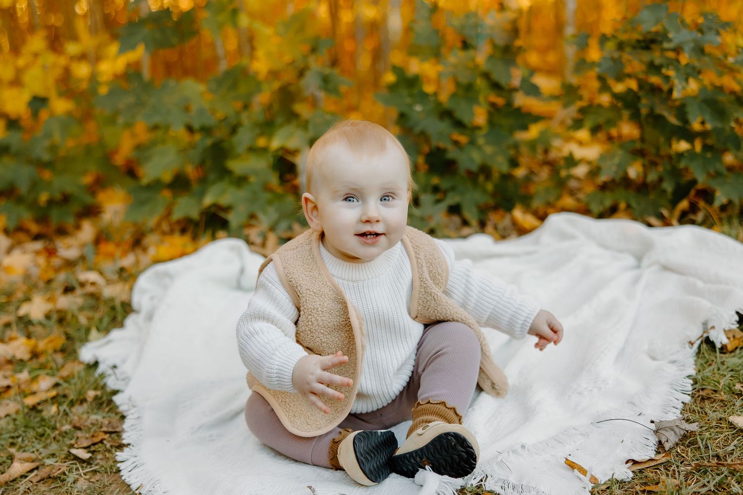 Baby in white clothing lying on blanket outdoors during autumn.