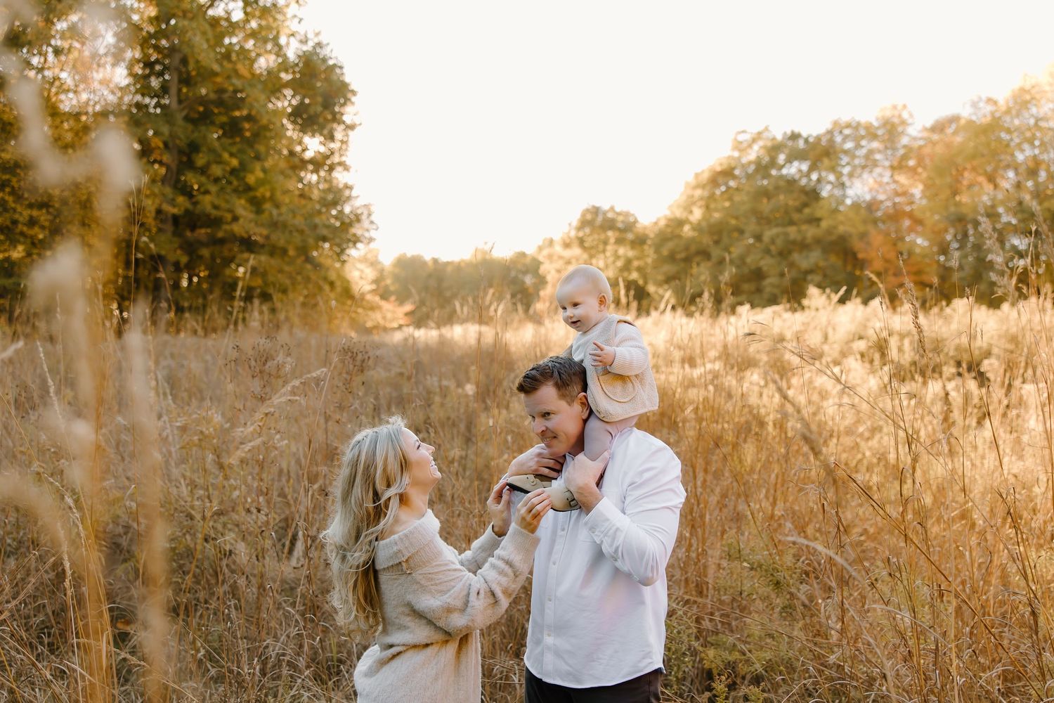 A family enjoys playful interactions in a sun-lit field of tall grass during golden hour.