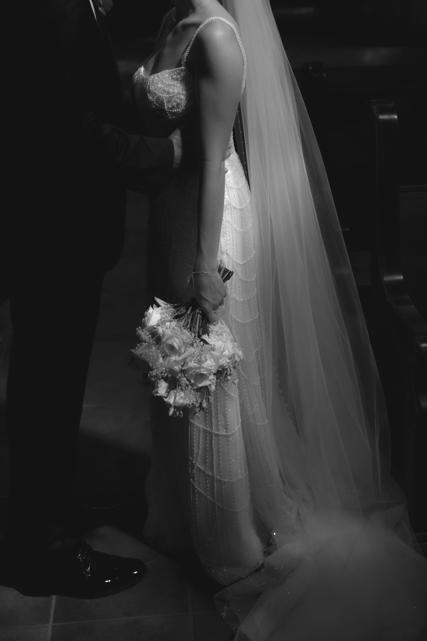 Artistic black and white side profile of bride holding bouquet with flowing veil.