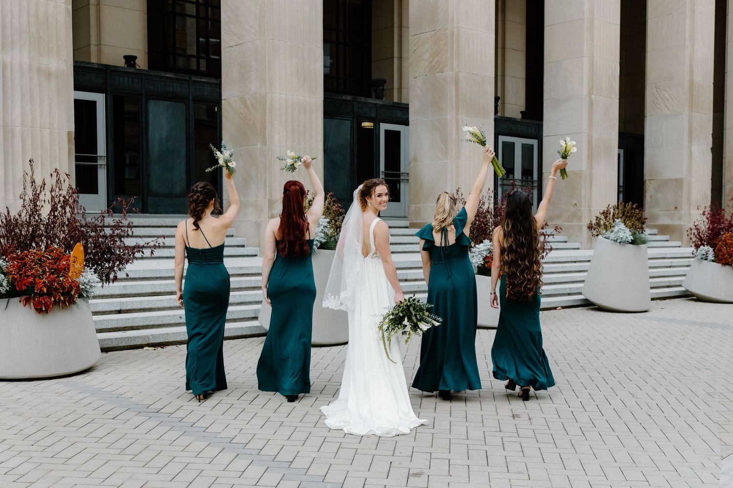 Elegant wedding party stands in front of classical stone columns and steps.