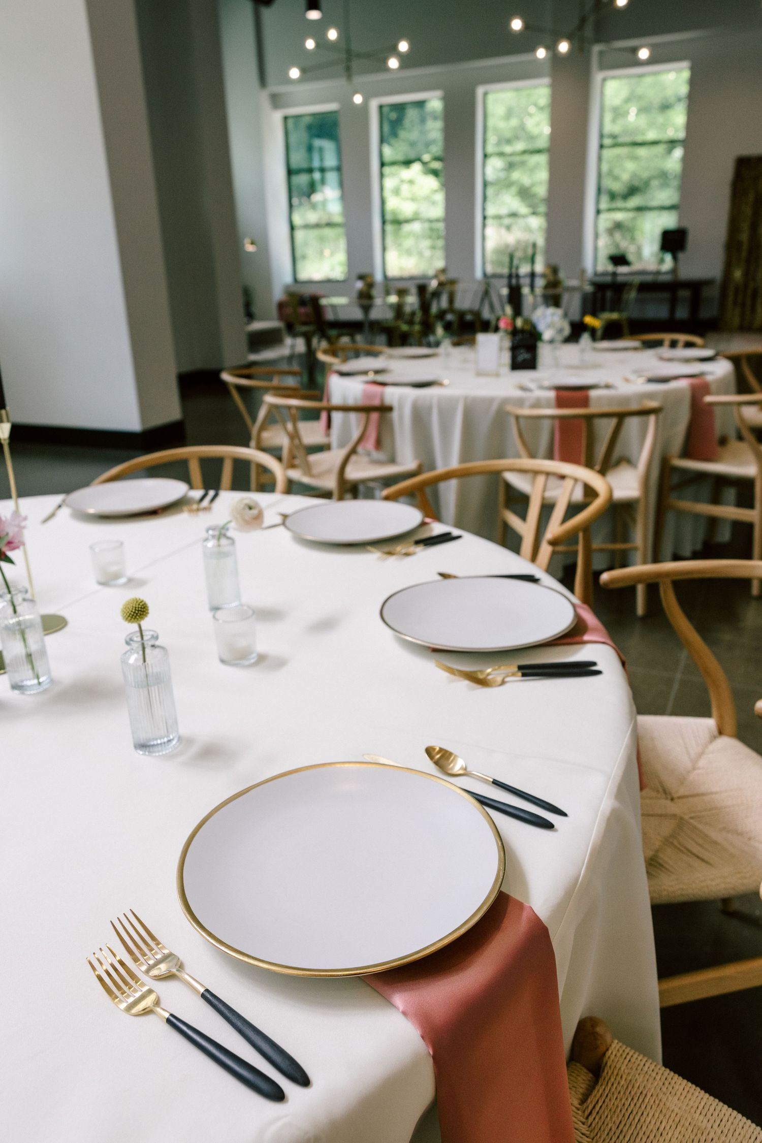 Elegant table settings with white plates, gold trim, and modern cutlery in a bright dining space.
