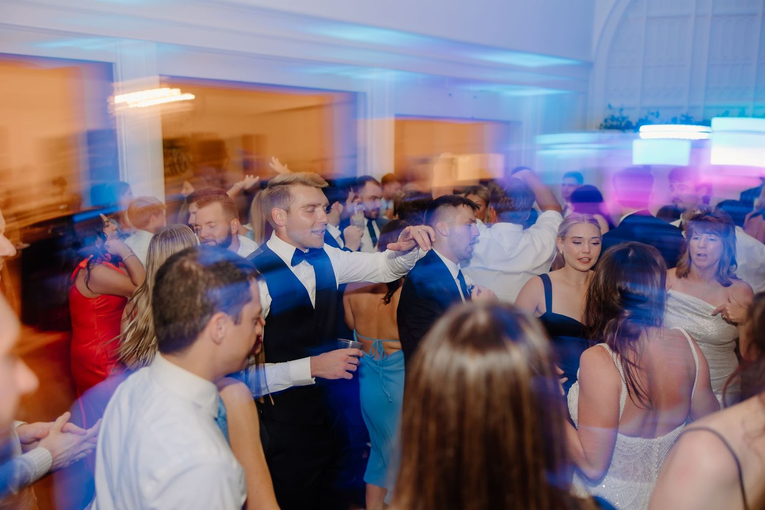 Crowded wedding dance floor with blue uplighting and guests enjoying the celebration.
