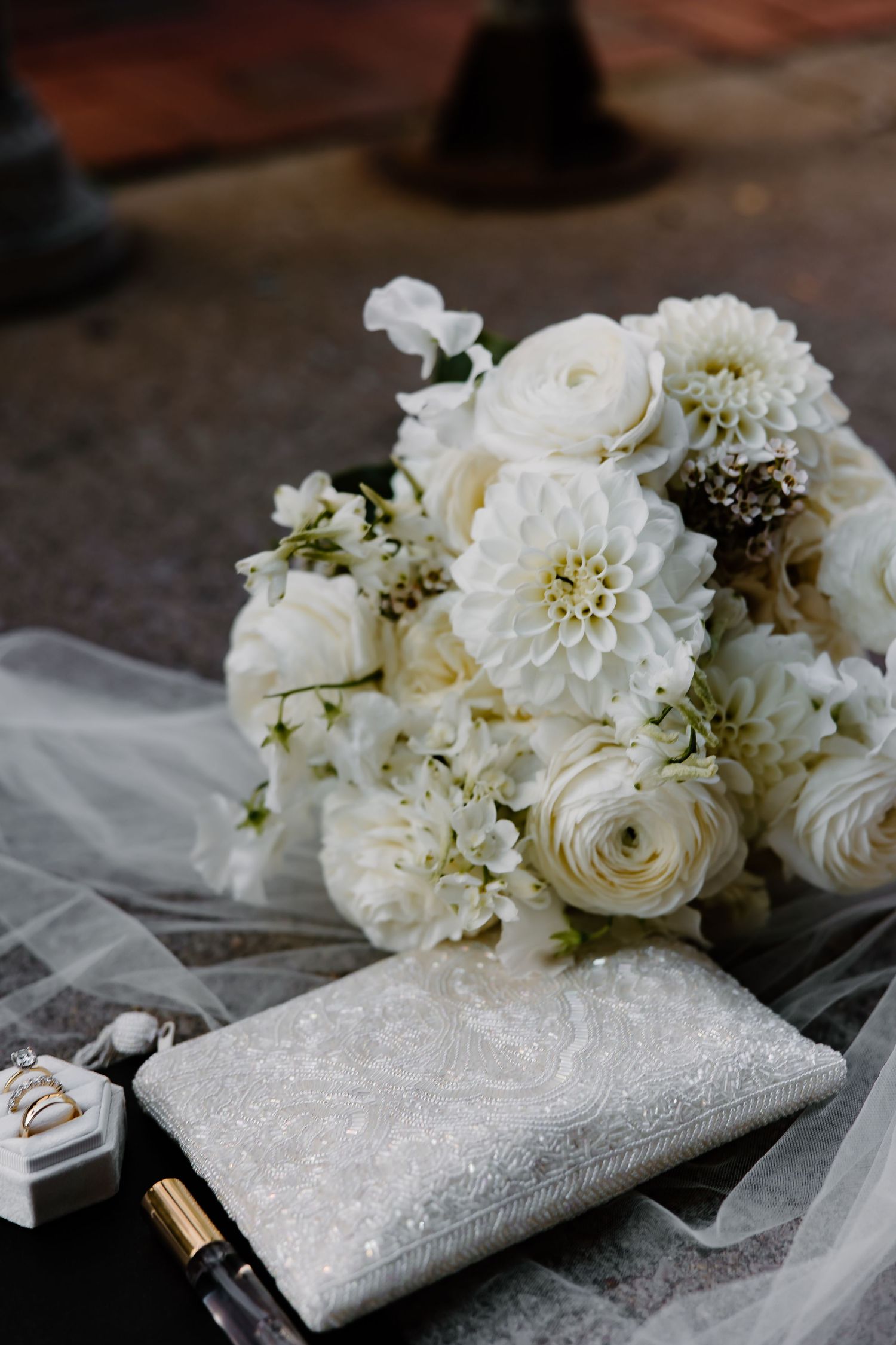 An elegant white bridal bouquet with roses and dahlias next to wedding accessories.