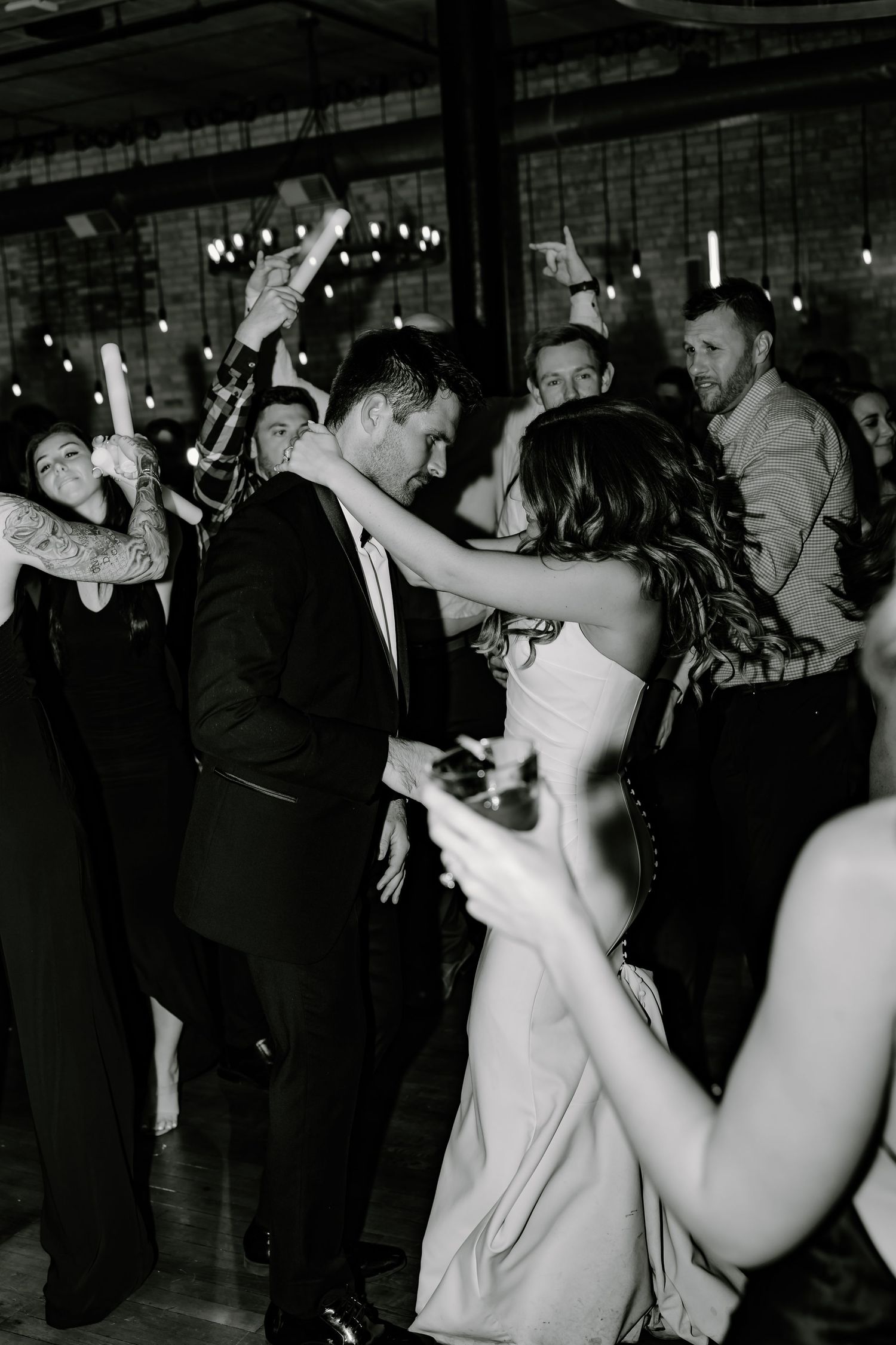 Black and white photo of wedding guests dancing at a lively reception.