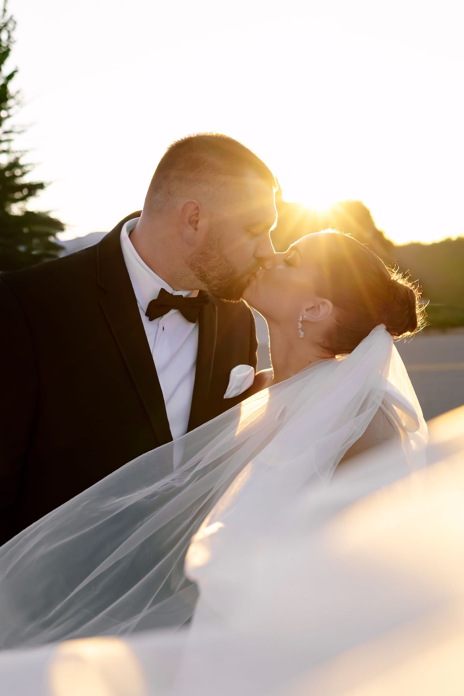 Golden sunset light creates silhouette of wedding couple with flowing veil.