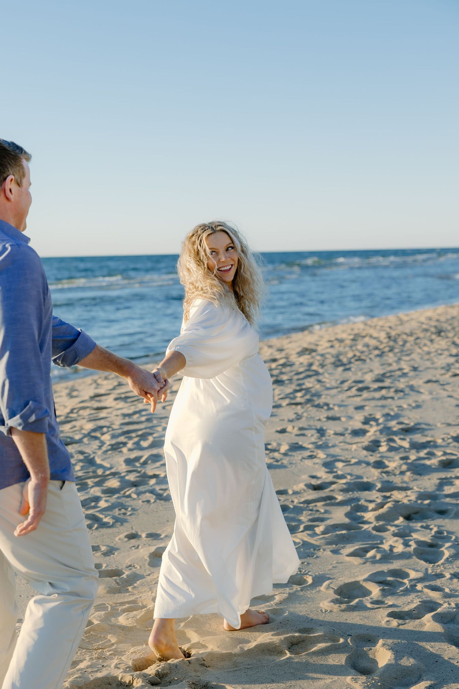 Two people in white outfits strolling along the shoreline with ocean waves in the background.