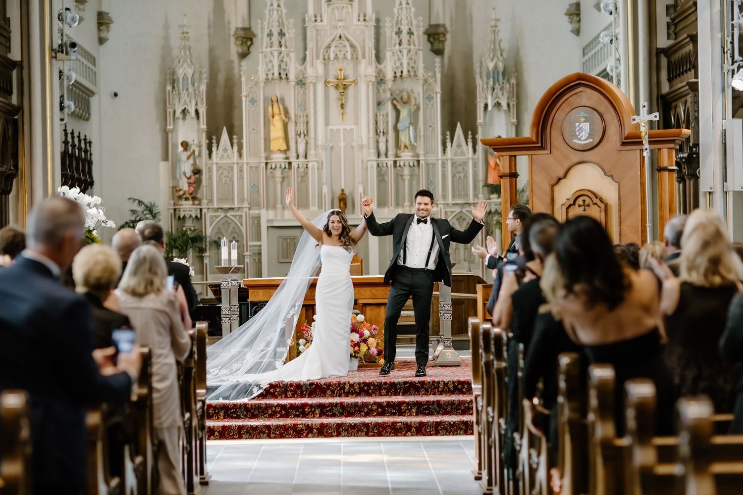 Cathedral wedding ceremony with guests seated in wooden pews under vaulted Gothic ceilings.