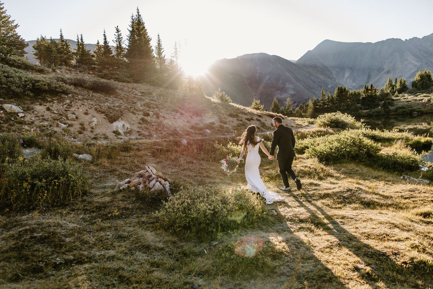A couple shares a romantic moment at sunset in a mountainous landscape with golden light and evergreen trees.