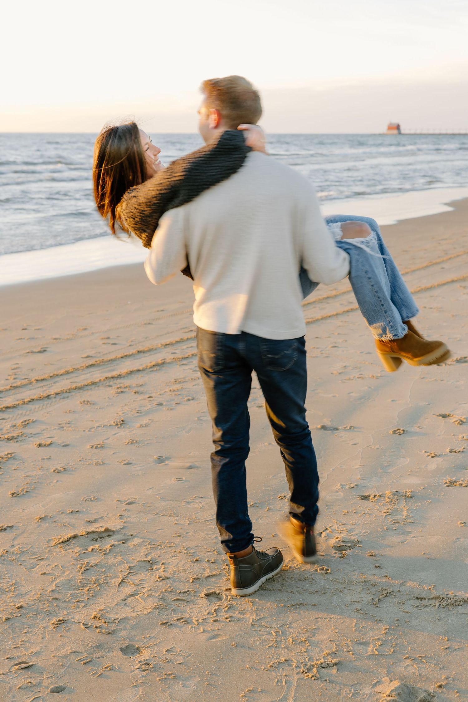 Playful couple dancing and spinning on a sandy beach at sunset.