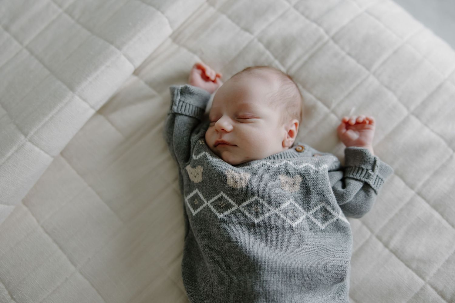 Close-up of sleeping baby wrapped in soft gray blanket on quilted white surface.
