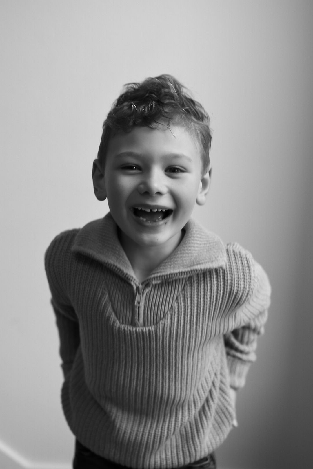 A joyful young boy in a ribbed sweater laughs in a black and white portrait photo.