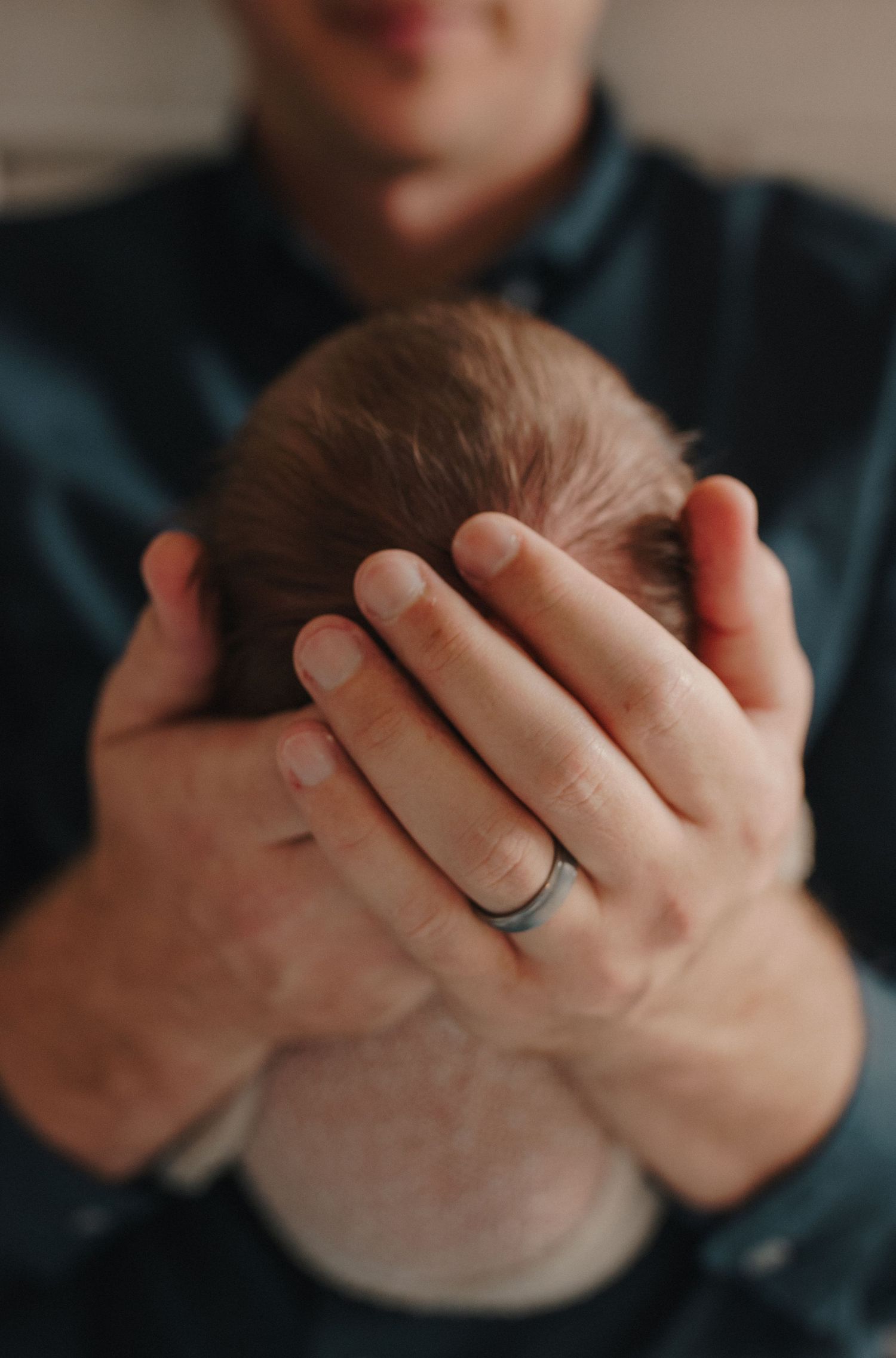 Father tenderly cradling newborn baby's head in both hands wearing a black silicone wedding ring.