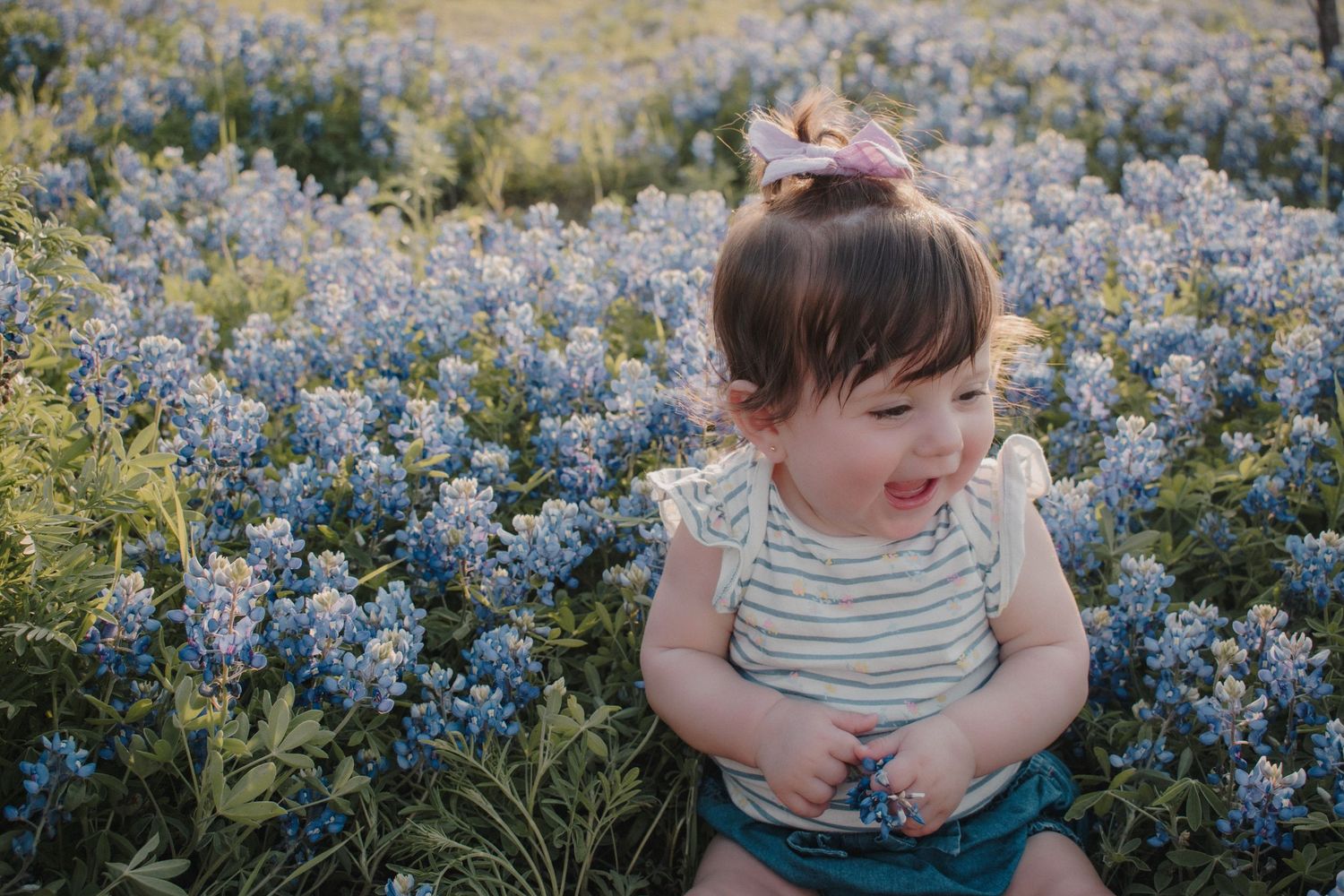 An adorable baby girl sits smiling in a vibrant field of blue wildflowers.