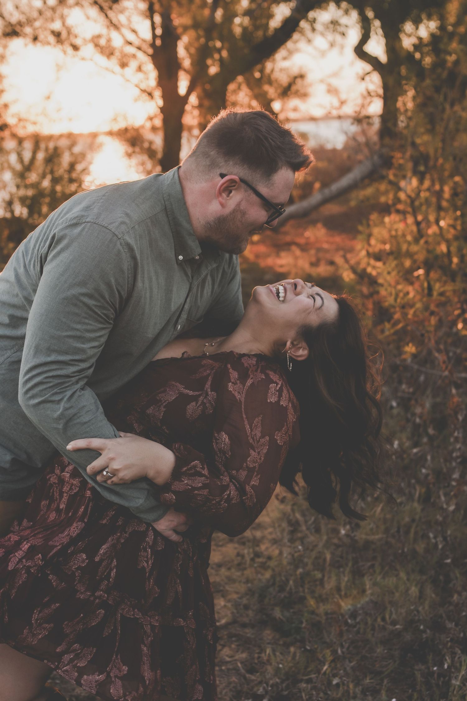Romantic couple laughing and dancing together in autumn forest during golden hour sunset.