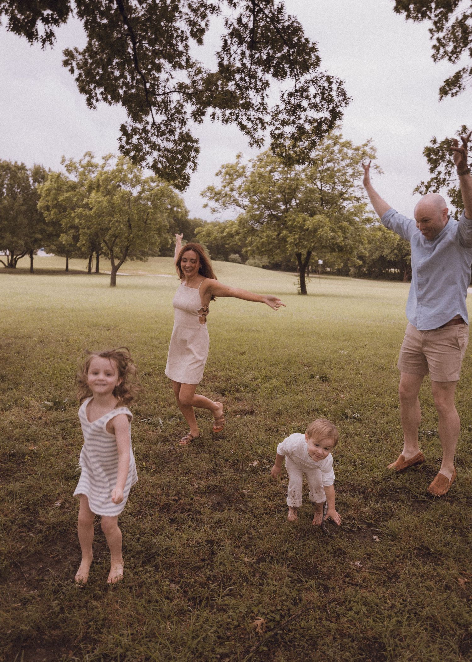 Family of four playing joyfully in a lush green park, parents and two young children enjoying outdoor fun.