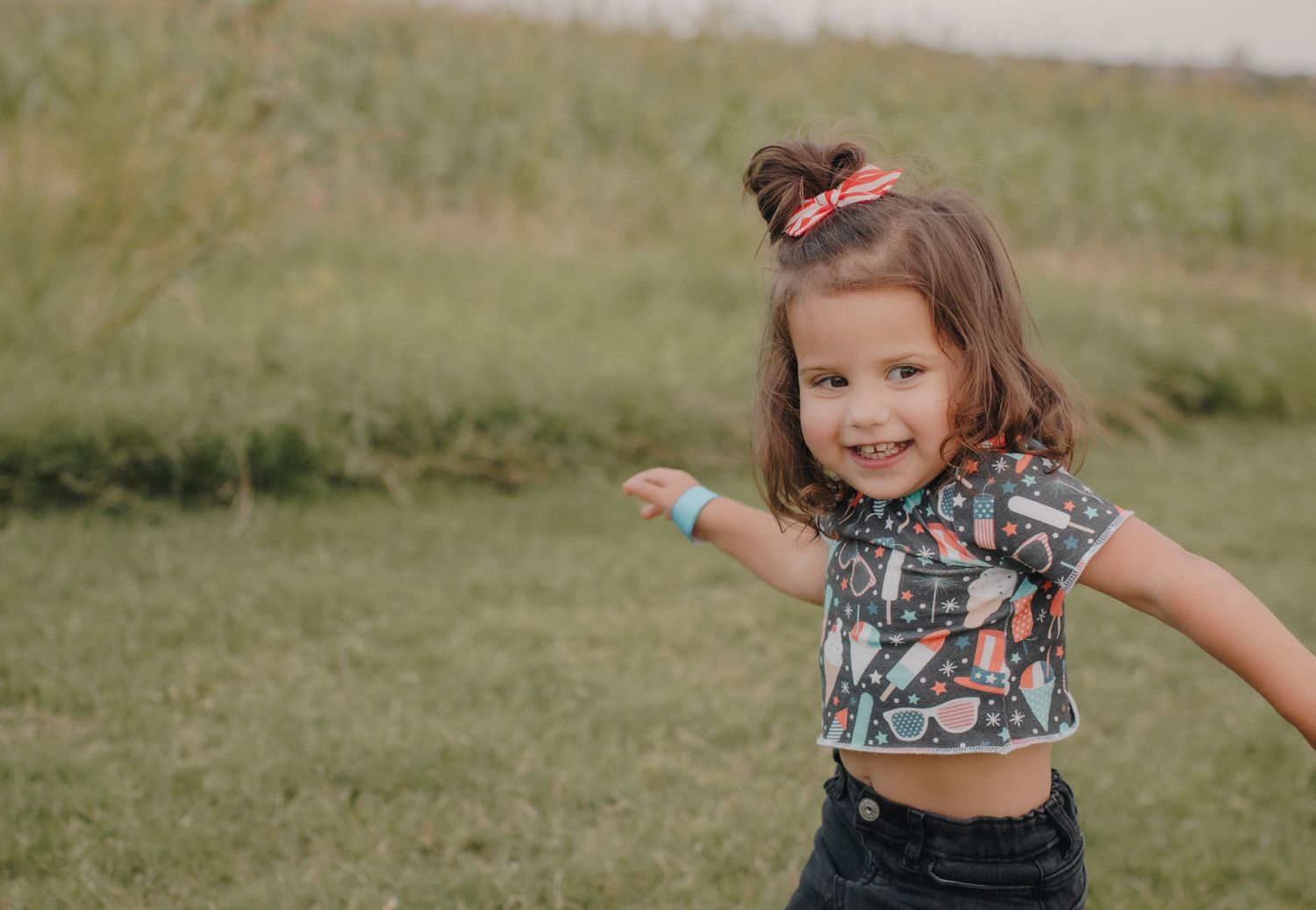 Smiling young girl in patterned crop top playing in green grassy field.