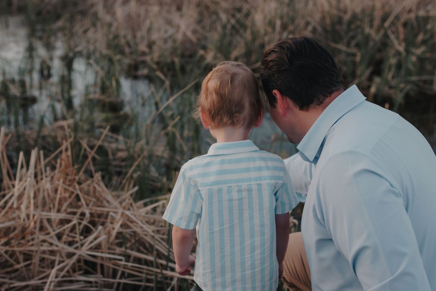 Father and young son bonding while looking at nature by a pond.