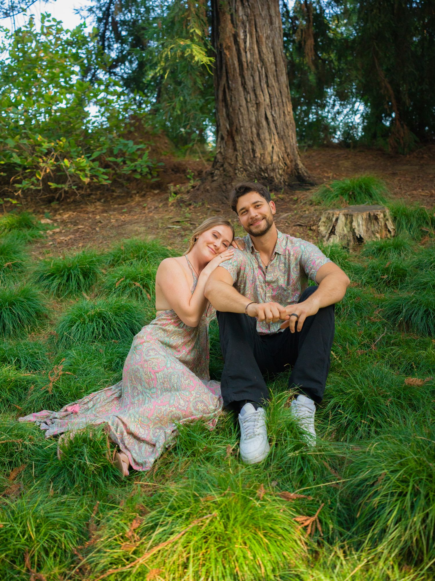 A couple relaxes together on lush grass during a romantic outdoor photoshoot at sunset.