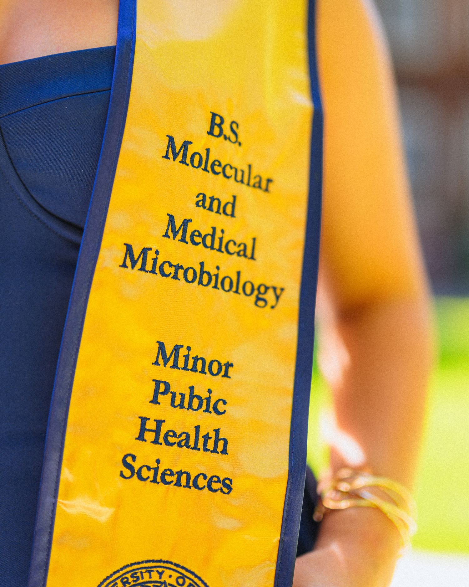 Close-up of gold graduation stoles showing Medical and Microbiology text details.
