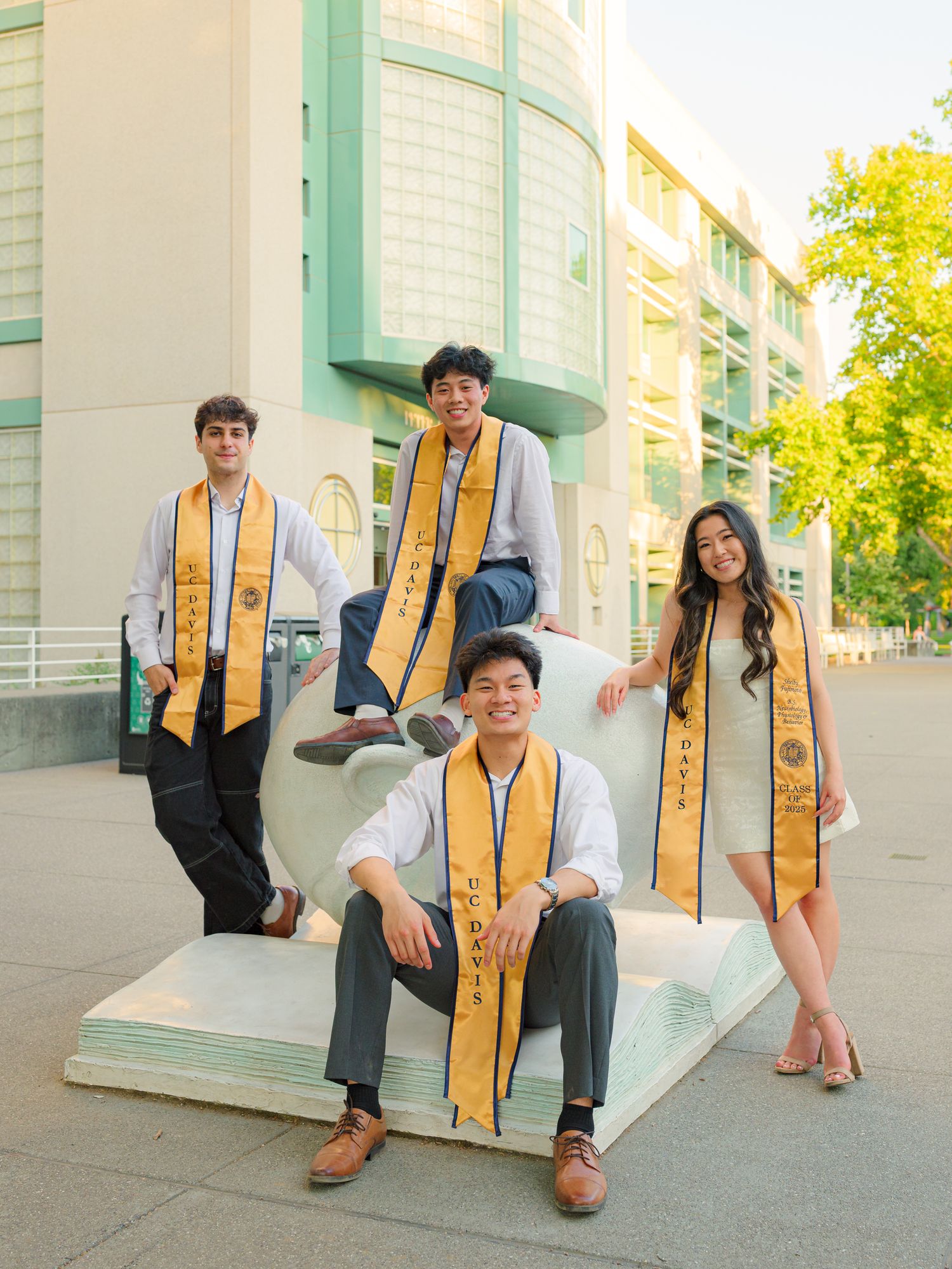 Creative graduation photos with gold stoles against a mint green building exterior.