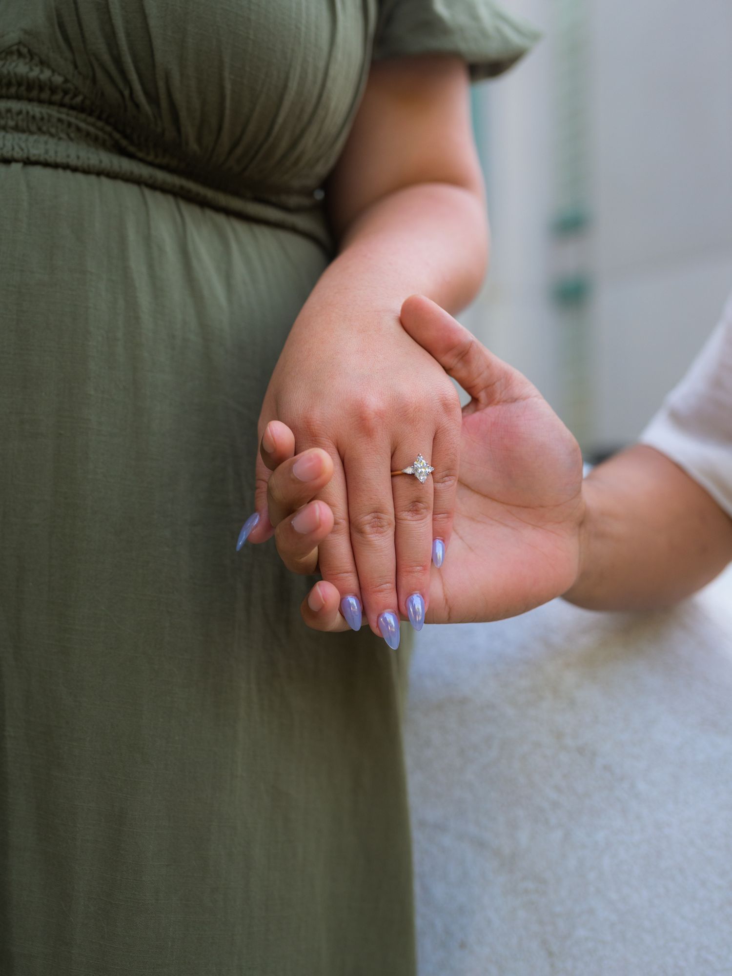 Close-up of hands with engagement ring against light colored background.