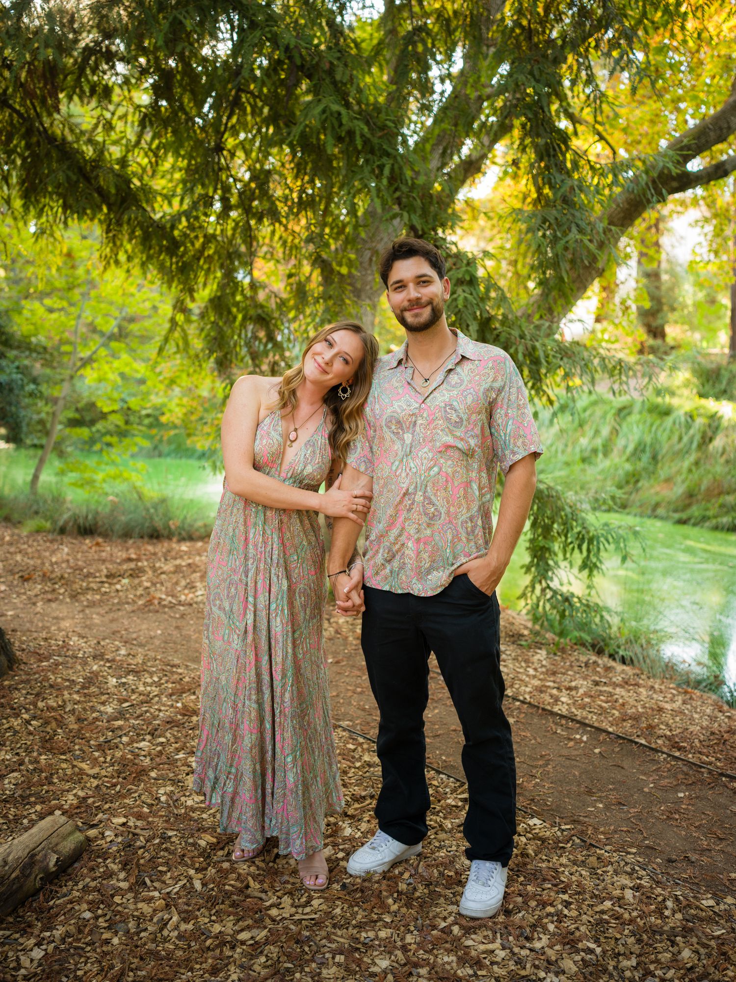 Couple poses playfully under tree branches during outdoor photo session.