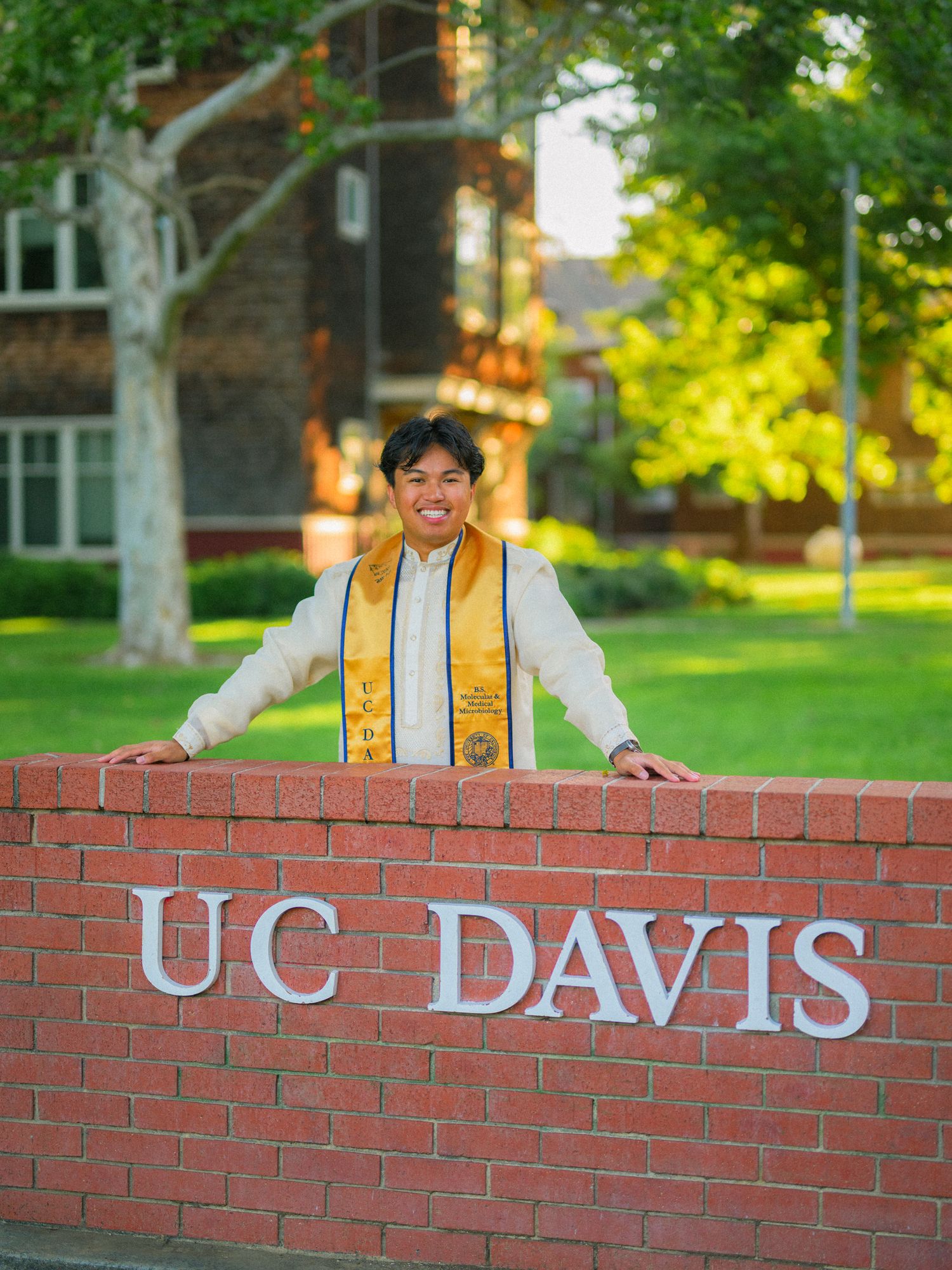 Graduate poses with UC Davis brick sign on campus during graduation photos.