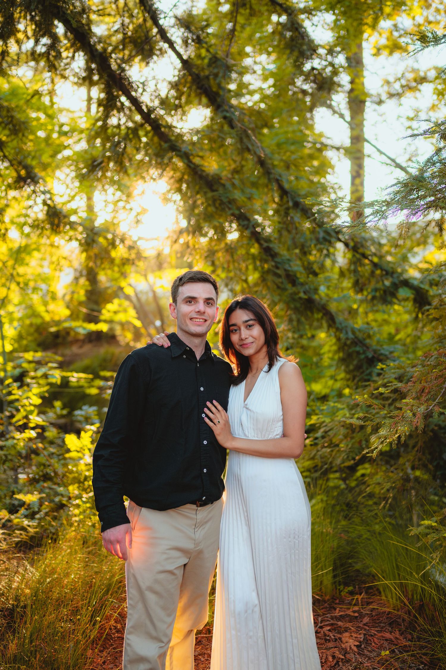 Engagement photos in a sunlit forest setting with golden hour lighting.