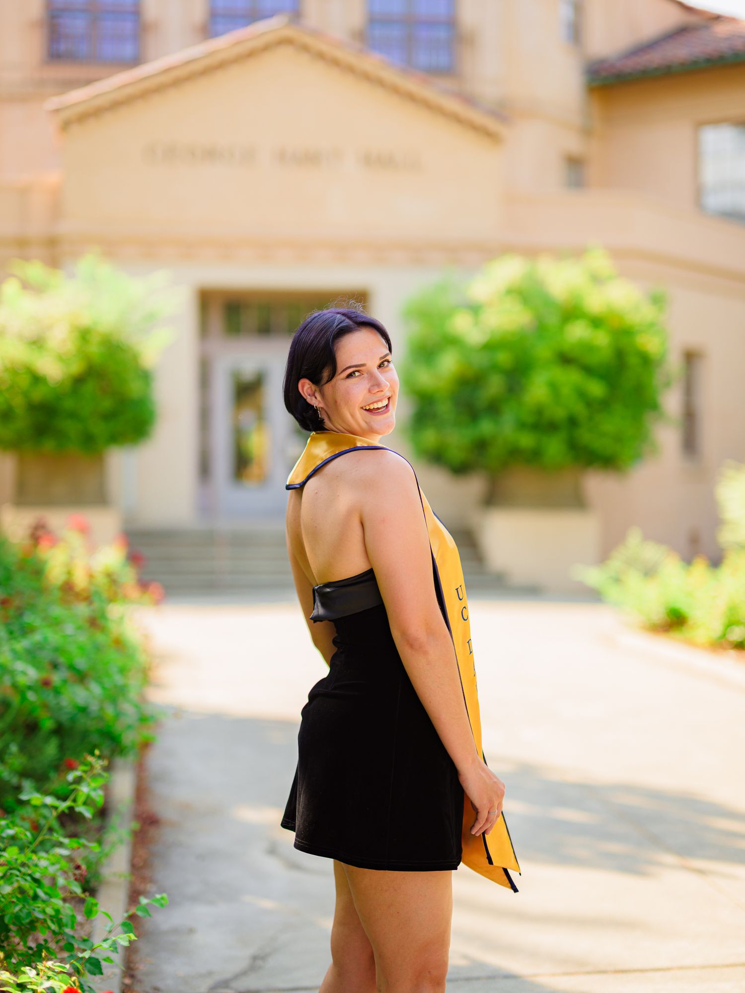 Graduate in a black dress poses in front of George Hart Hall building during graduation photoshoot.