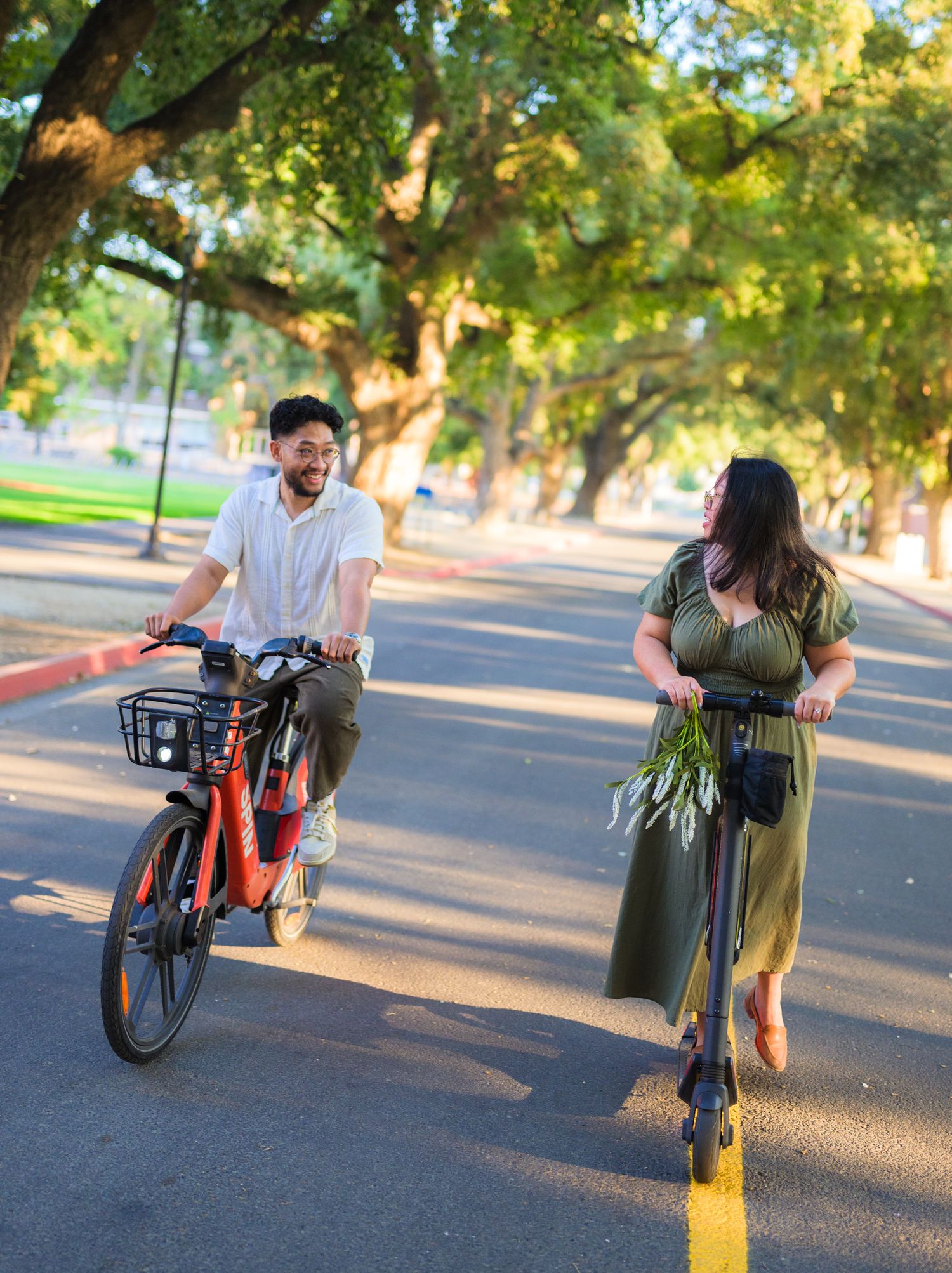 Couple poses with bicycle in late afternoon sunlight on paved path.