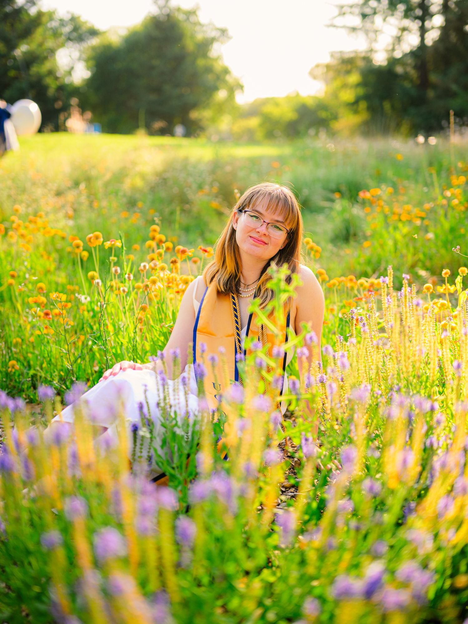 Graduate lying in field of purple and yellow wildflowers during golden hour.
