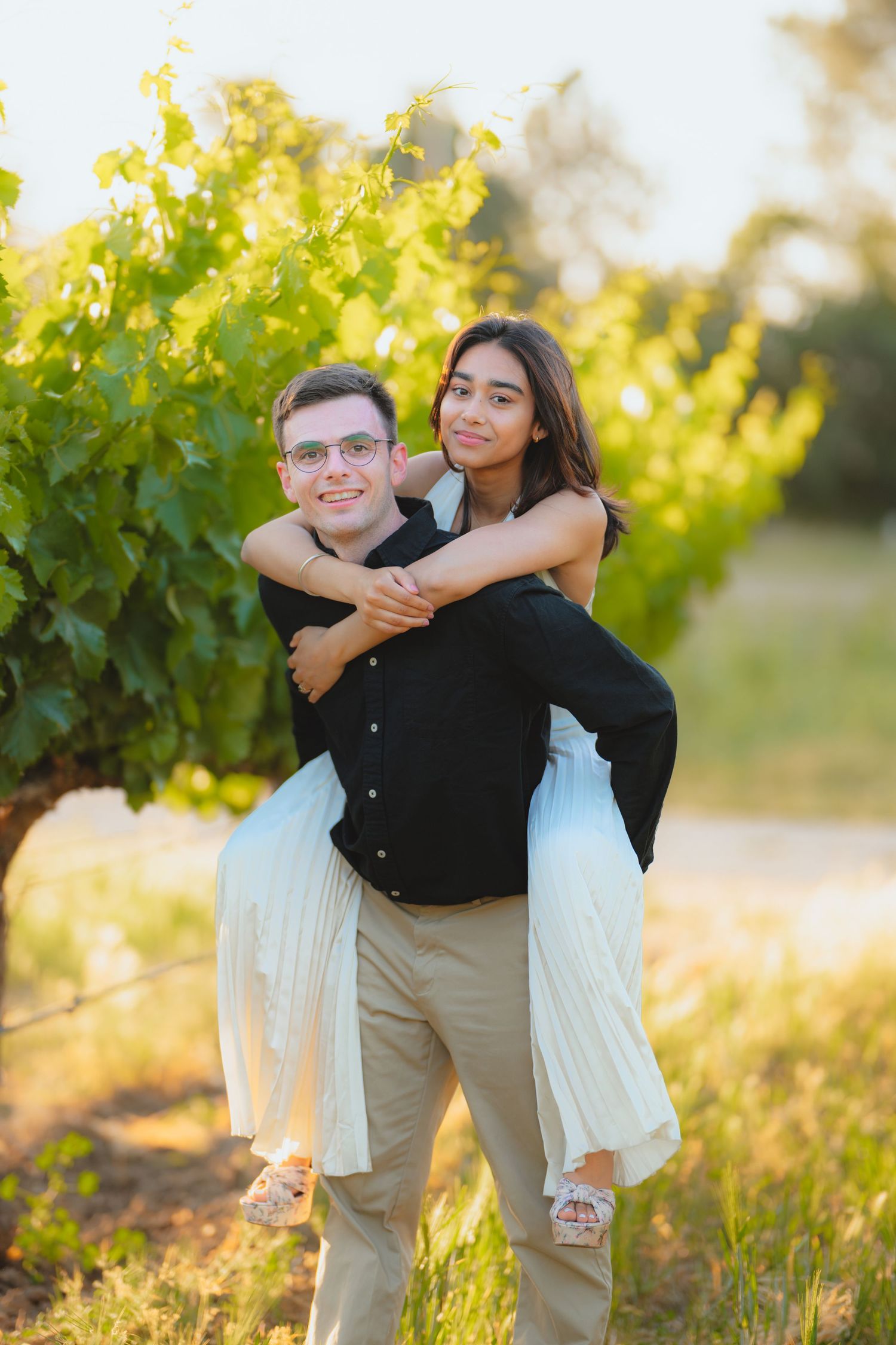 Playful engagement photos taken in a sunny vineyard setting.