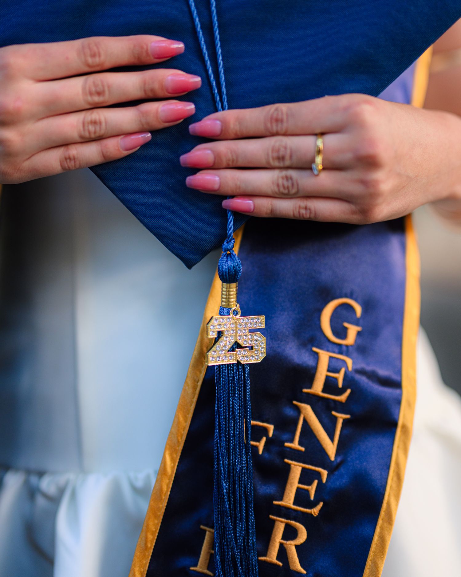 Close-up of hands touching graduation stoles with gold trim against blue fabric.