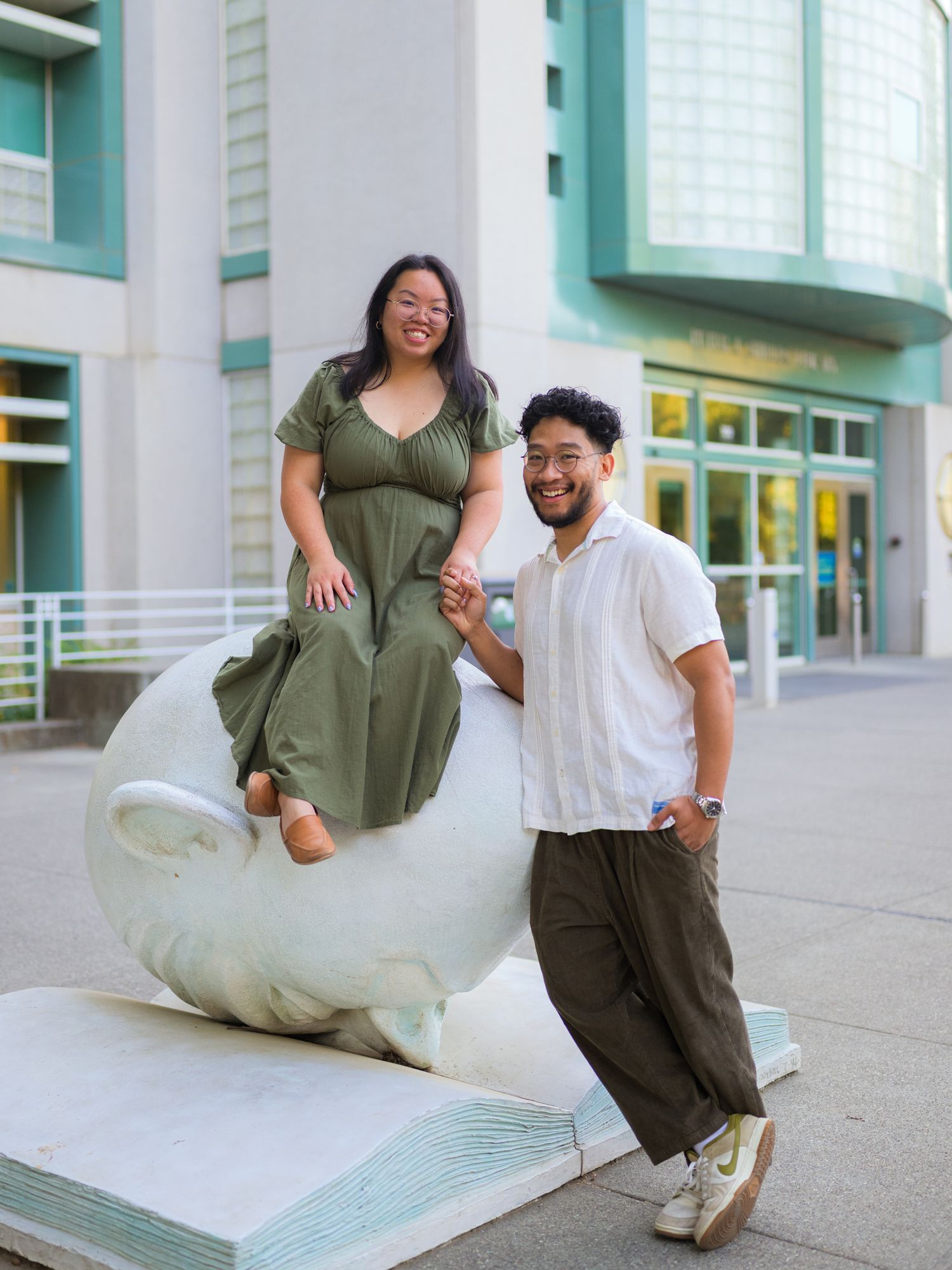 Playful graduation photos taken outside a modern building with teal accents.