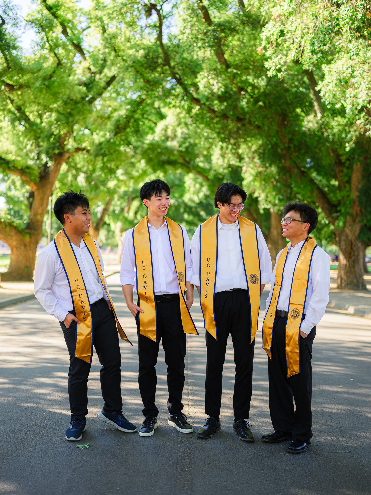 Graduates in black and gold stoles arranged in creative poses outdoors.