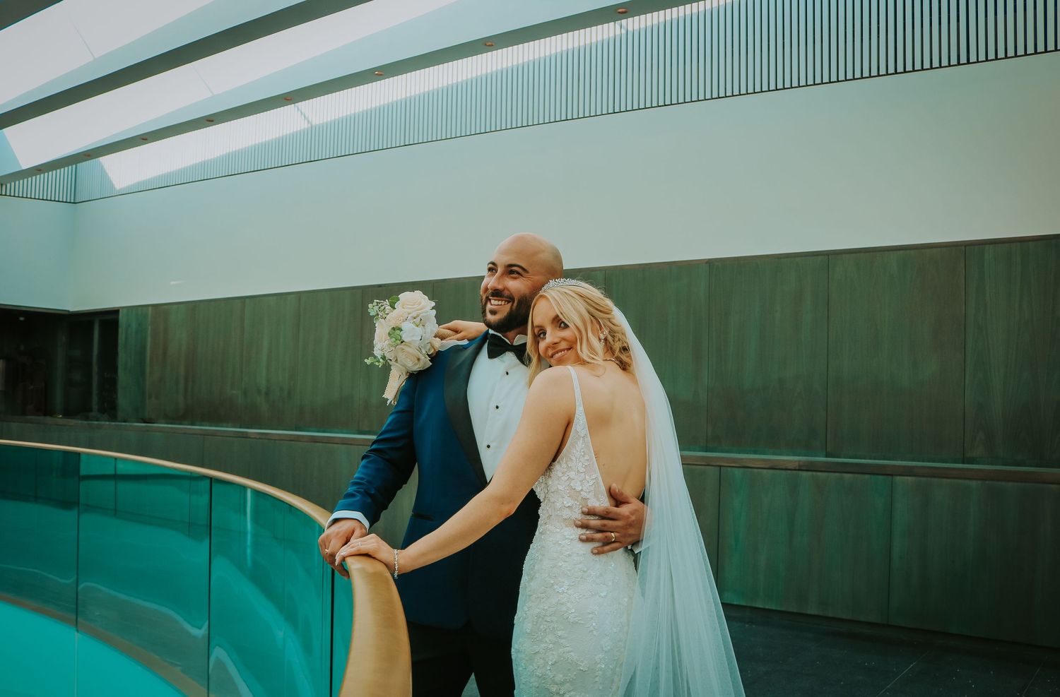 A couple pose together in an elegant architectural setting with turquoise accents at their wedding.
