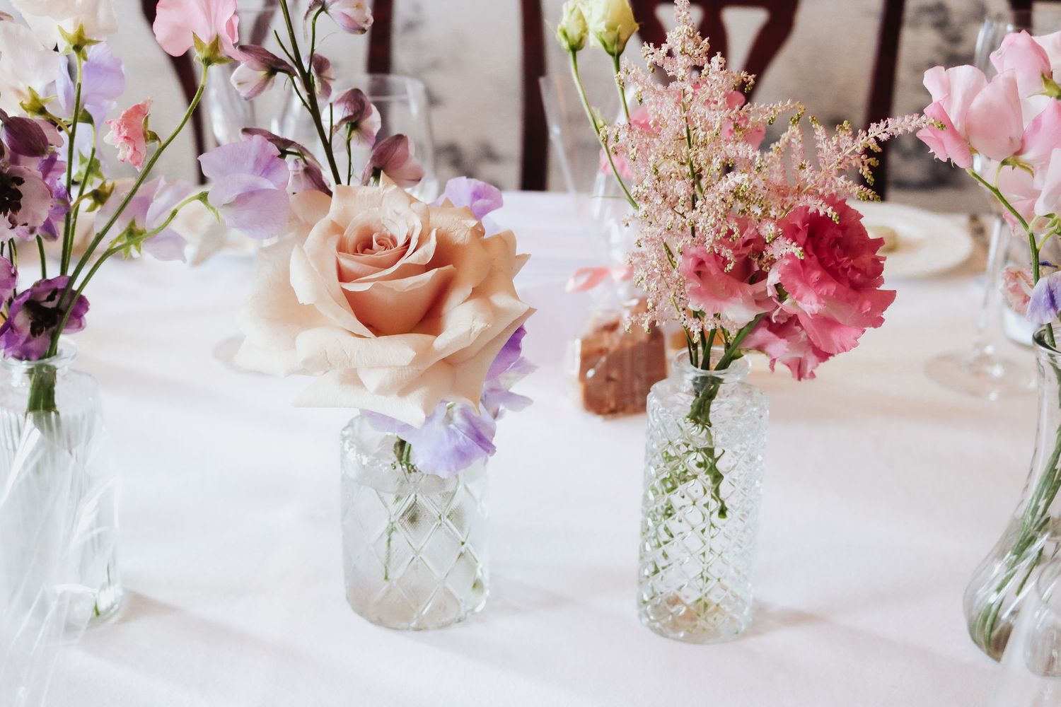 Delicate pink and peach roses arranged in vintage glass bottles on a white tablecloth for a romantic table setting.